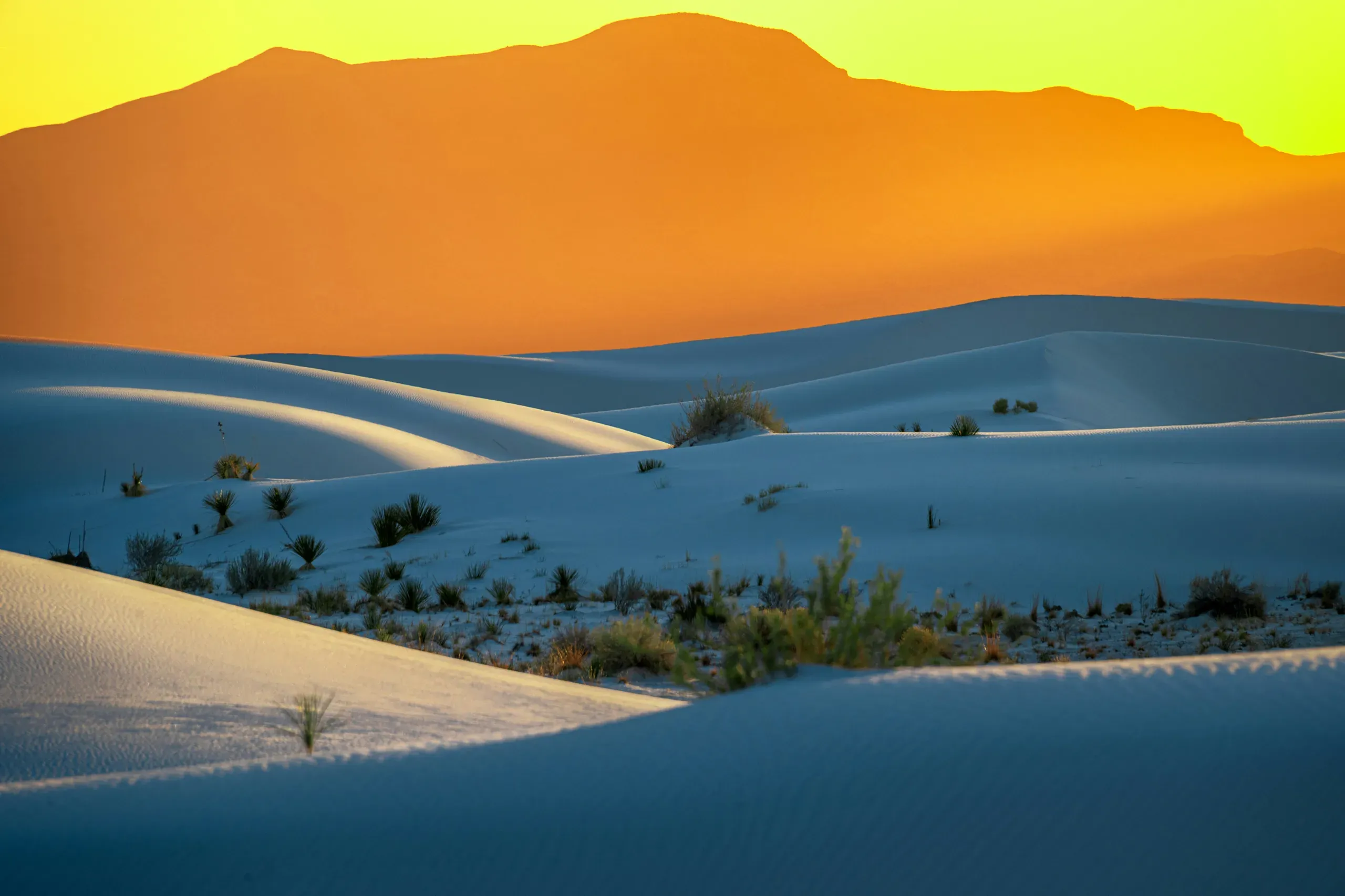 A breathtaking view of the pristine white sand dunes at White Sands National Park, with mountains in the distance under a clear sky at golden hour.