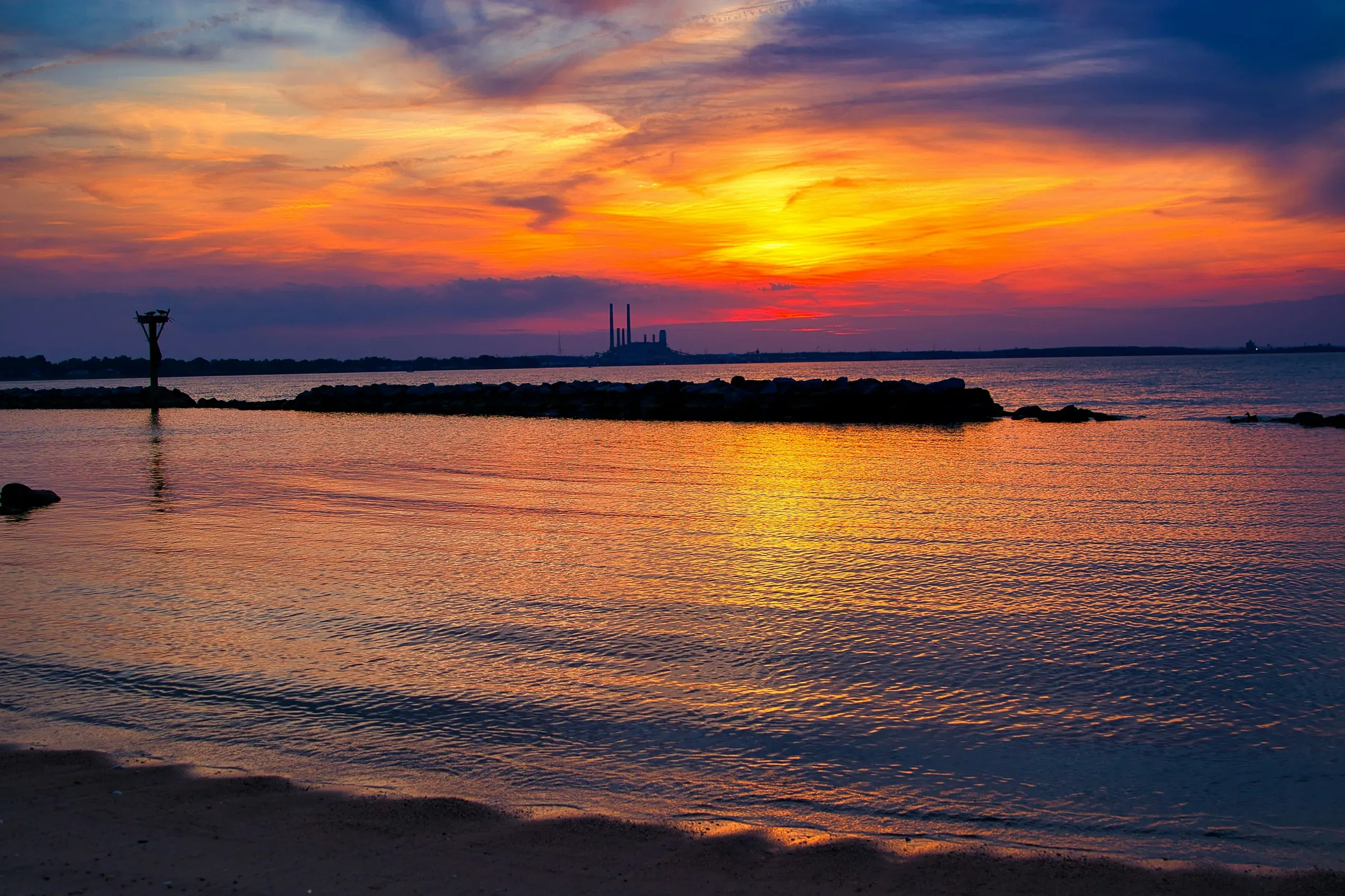 Sunset over the water at Fort Smallwood Road, Pasadena, Maryland, with birds nesting and a factory in the distance