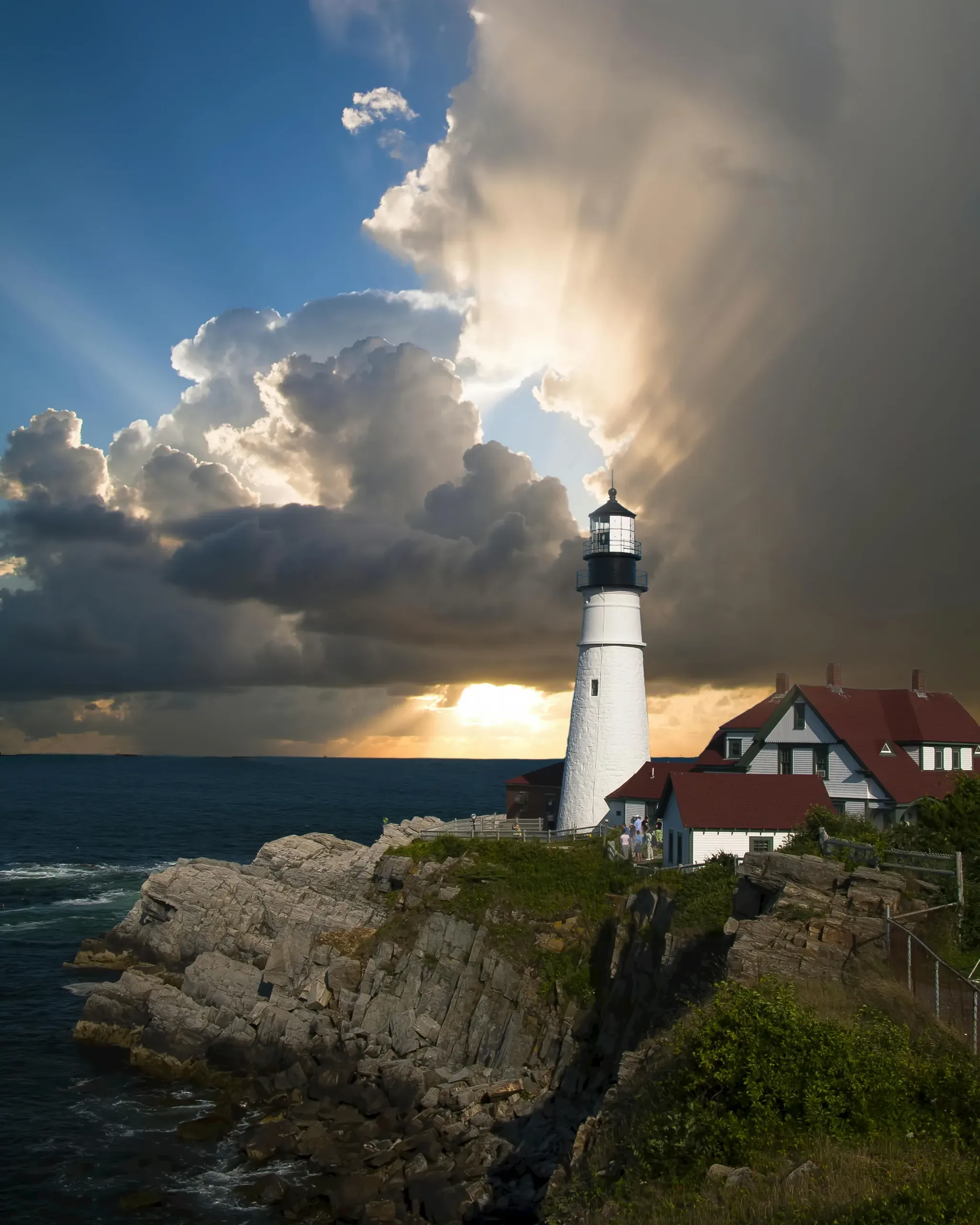 The Portland Head Light, a white and black lighthouse, stands on a rocky cliff next to a keepers' house in Cape Elizabeth, Maine.