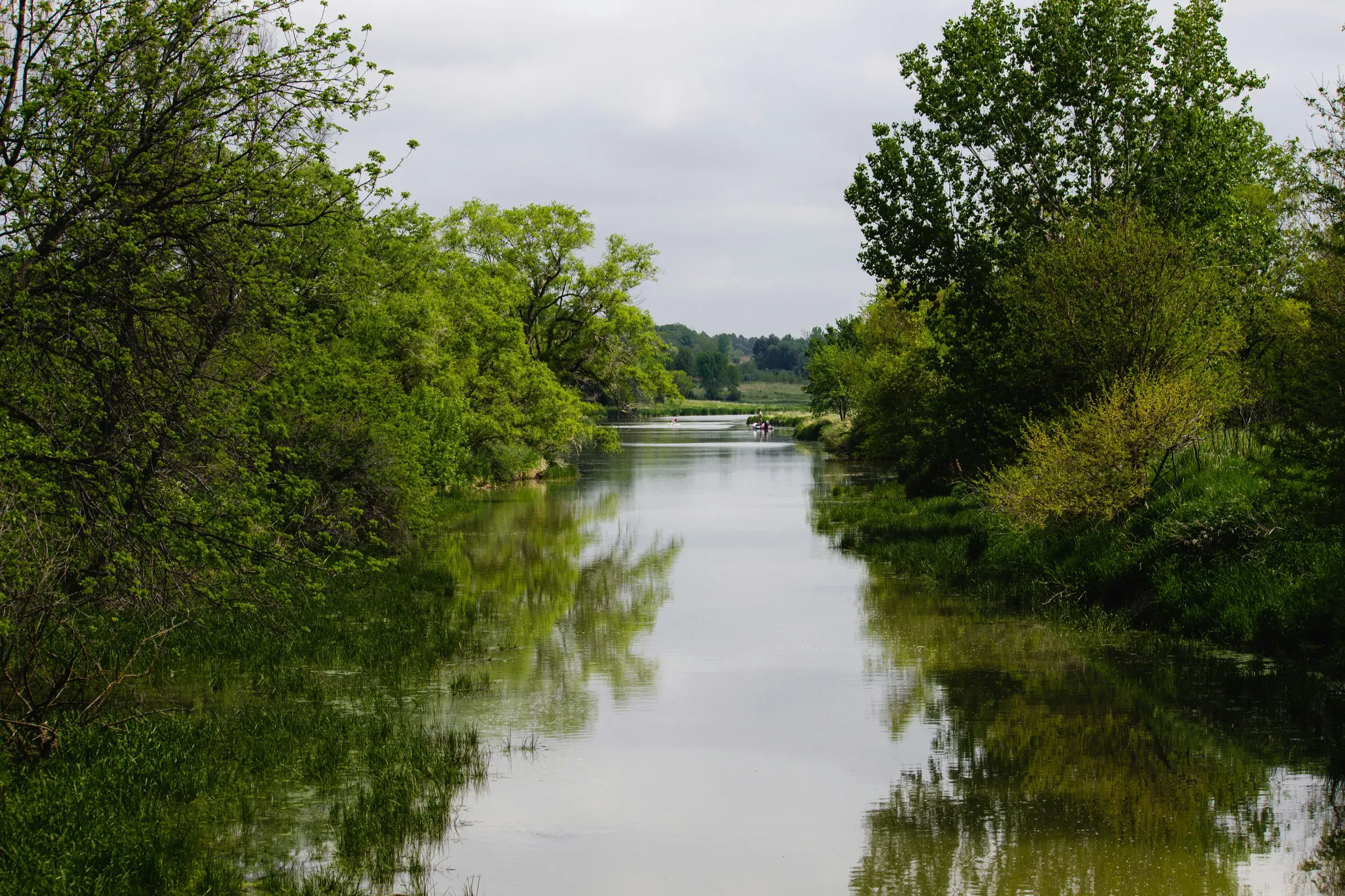 A river flowing into Wehrspan Lake with a fisherman and a kayaker, Omaha, Nebraska