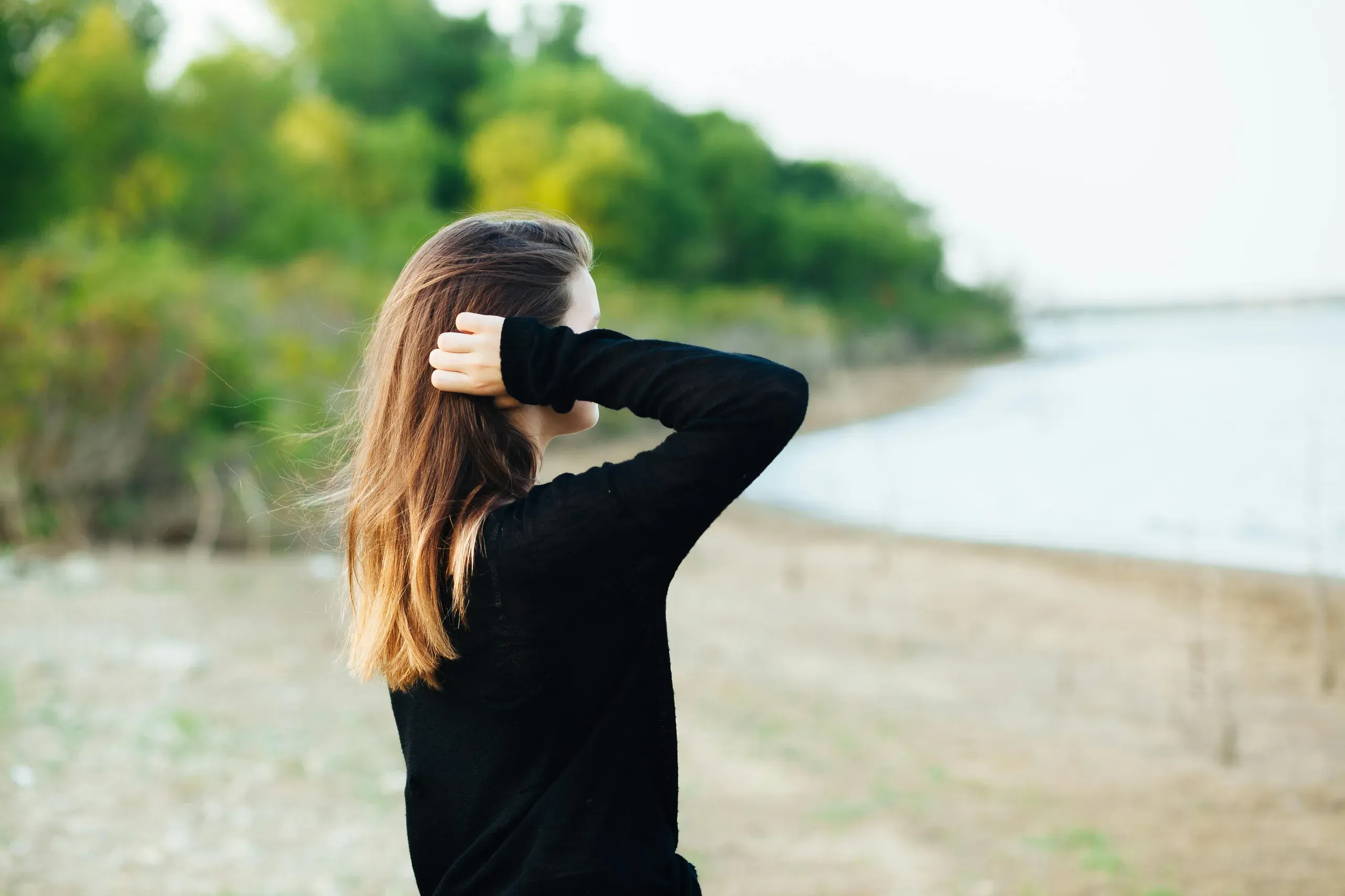 Oak Point, Texas. Woman wears black long-sleeved shirt standing near body of water