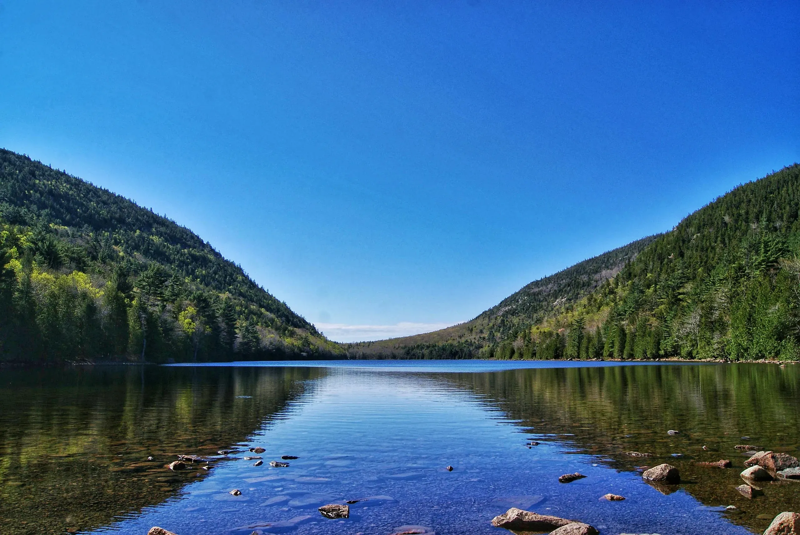 A beautiful mountain lake landscape under a clear blue sky in Maine.