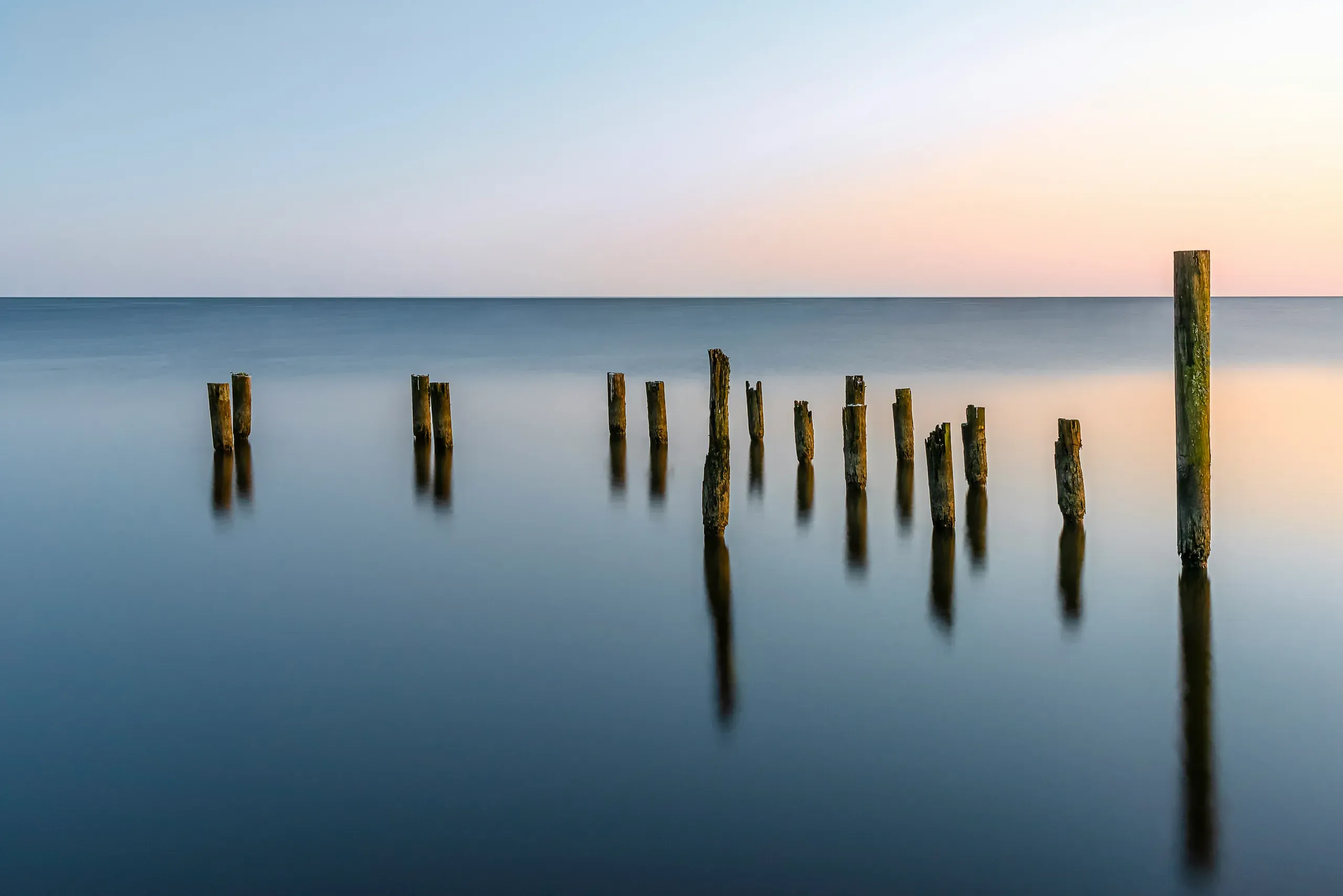 A line of weathered wooden pilings stands in the Tchefuncte River during a vibrant sunset in Madisonville, Louisiana.