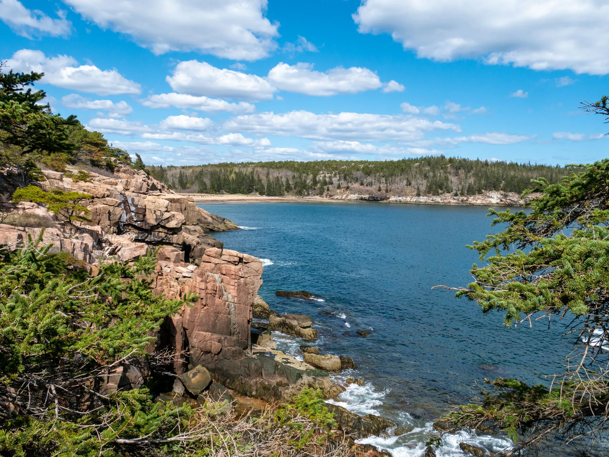A calm body of water in Acadia National Park is surrounded by rocks and autumn-coloured trees under a cloudy sky.