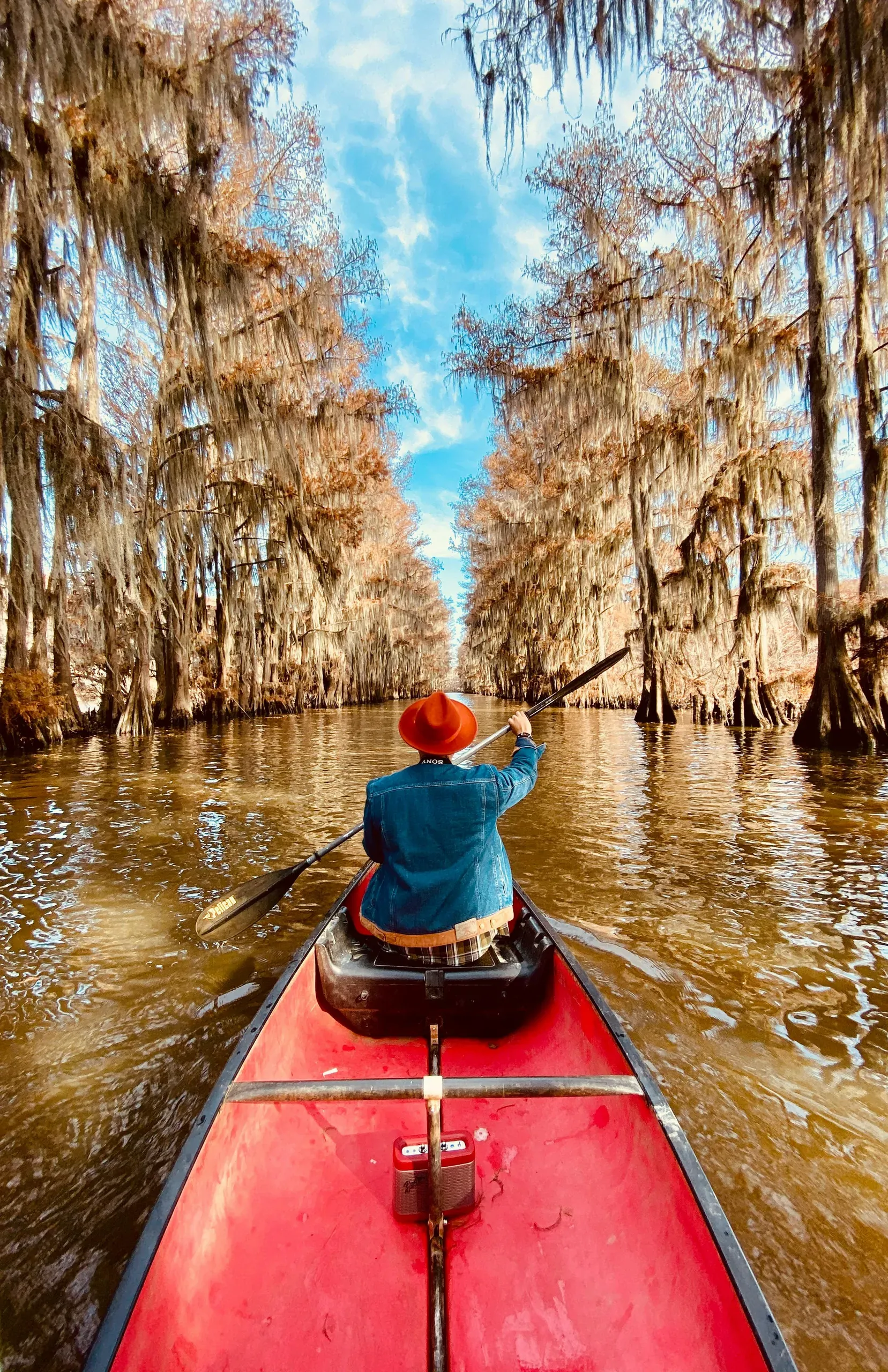 Karnack, Texas. Person wearing blue denim jacket riding red canoe boat