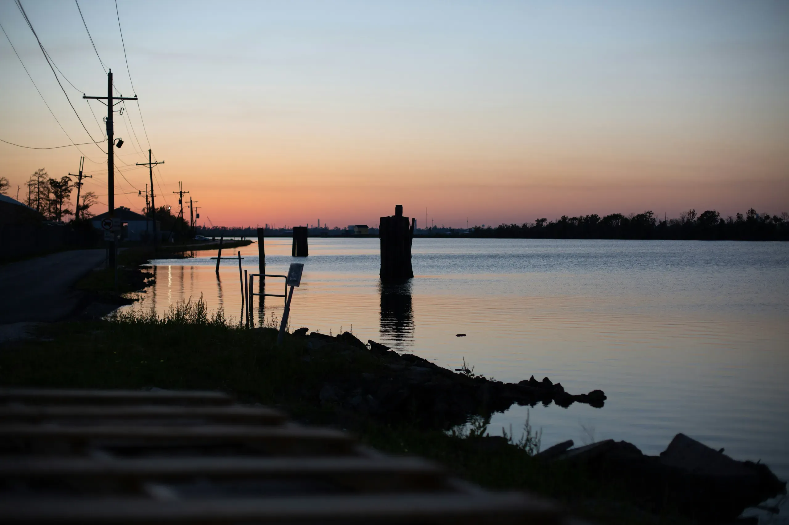 A wooden dock extends into a calm body of water, silhouetted against the colorful sky of a Louisiana sunset.