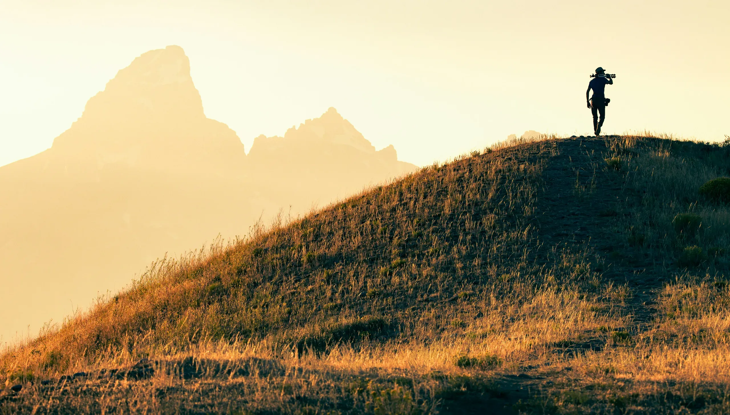 Grand Teton, Wyoming. Silhouette of a man climbing a hill at sunset in front of Grand Teton Mountains