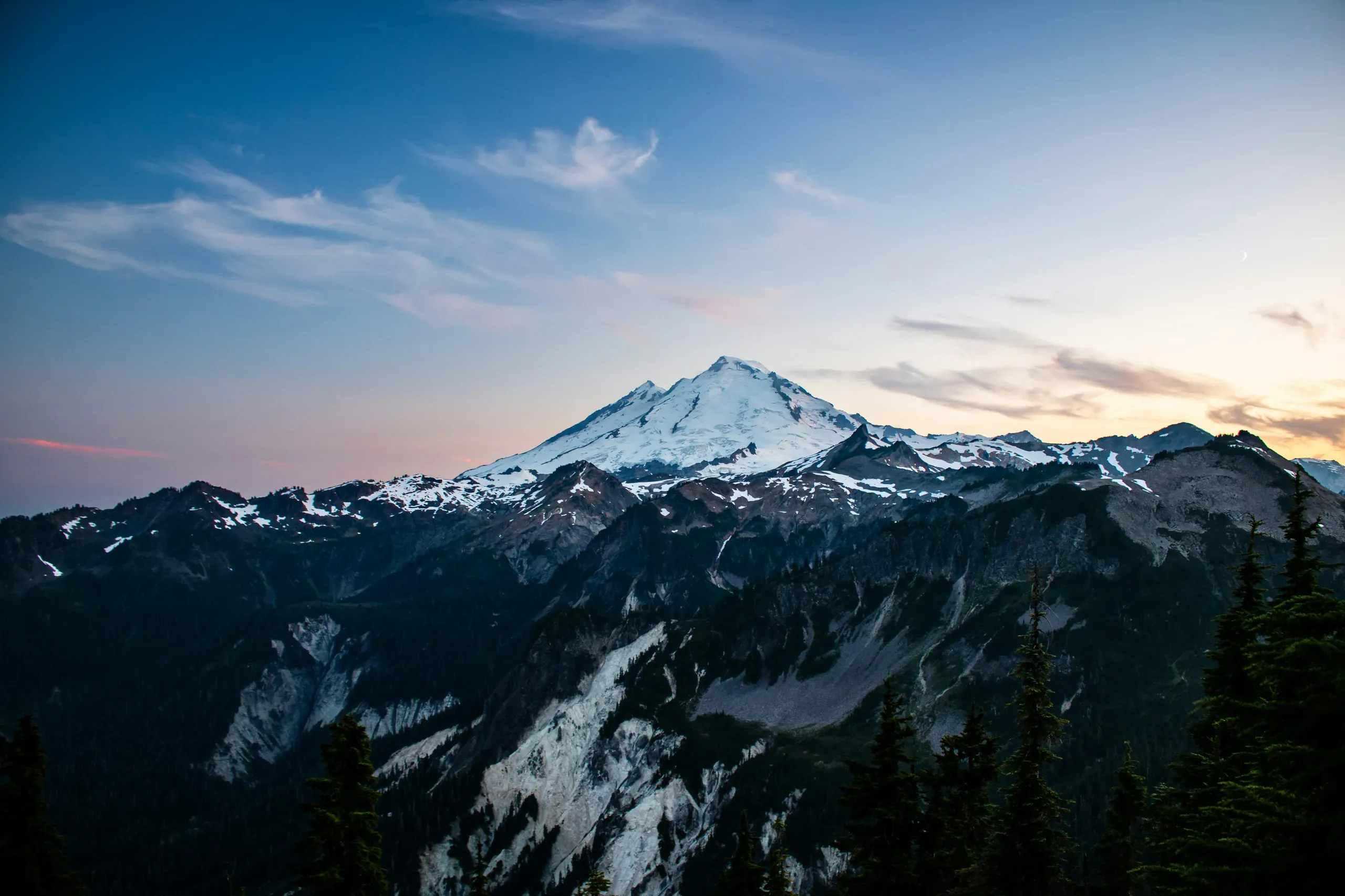 Huntoon Point, Washington. A stunning view of Mount Baker captured from Huntoon Point along Artist Ridge. The snow-covered peak of Mount Baker rises dramatically against a sunset sky, its rugged slopes blanketed in snow even during the warmer months.