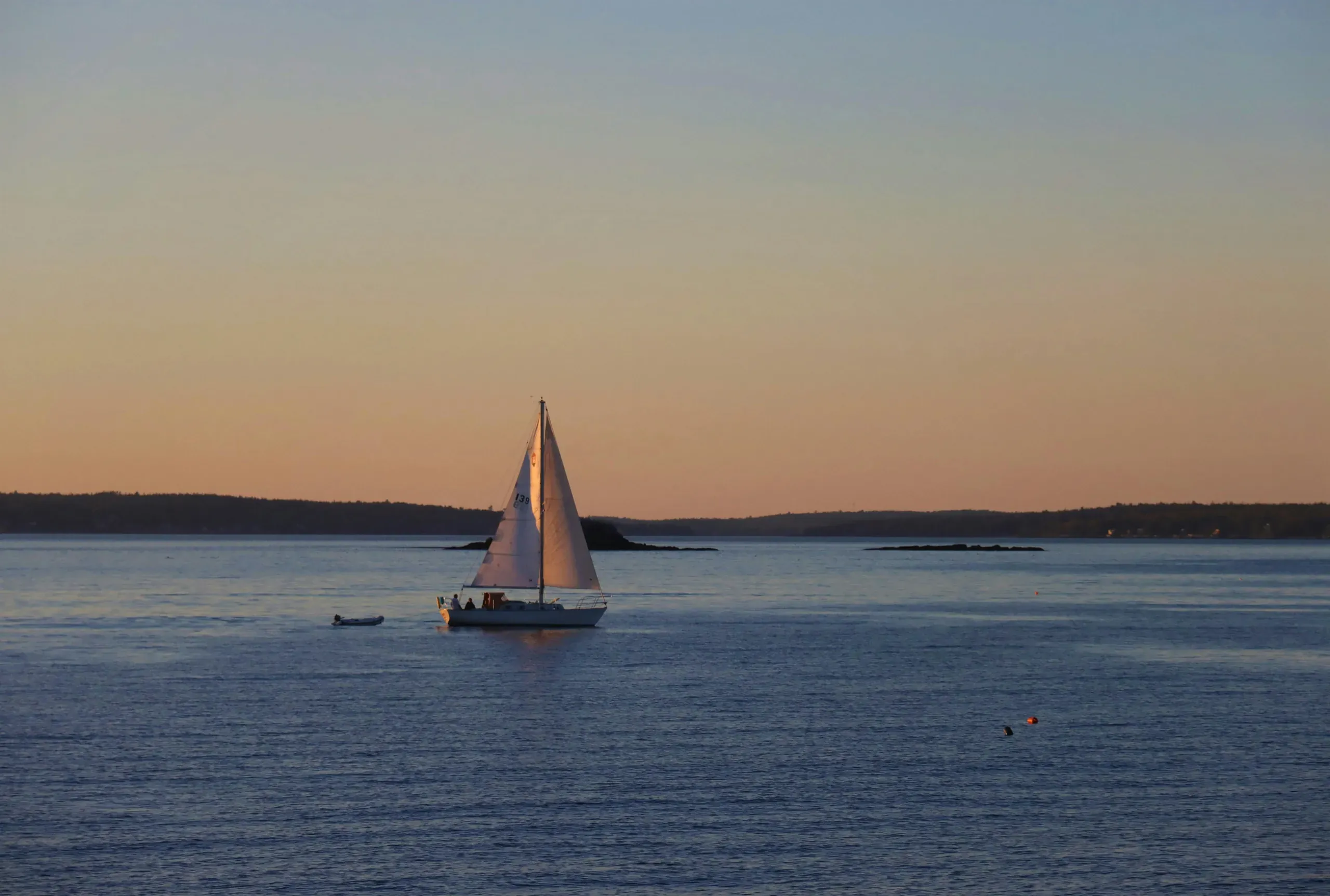 A sailboat is silhouetted on the sea against a vibrant sunset sky in Maine.