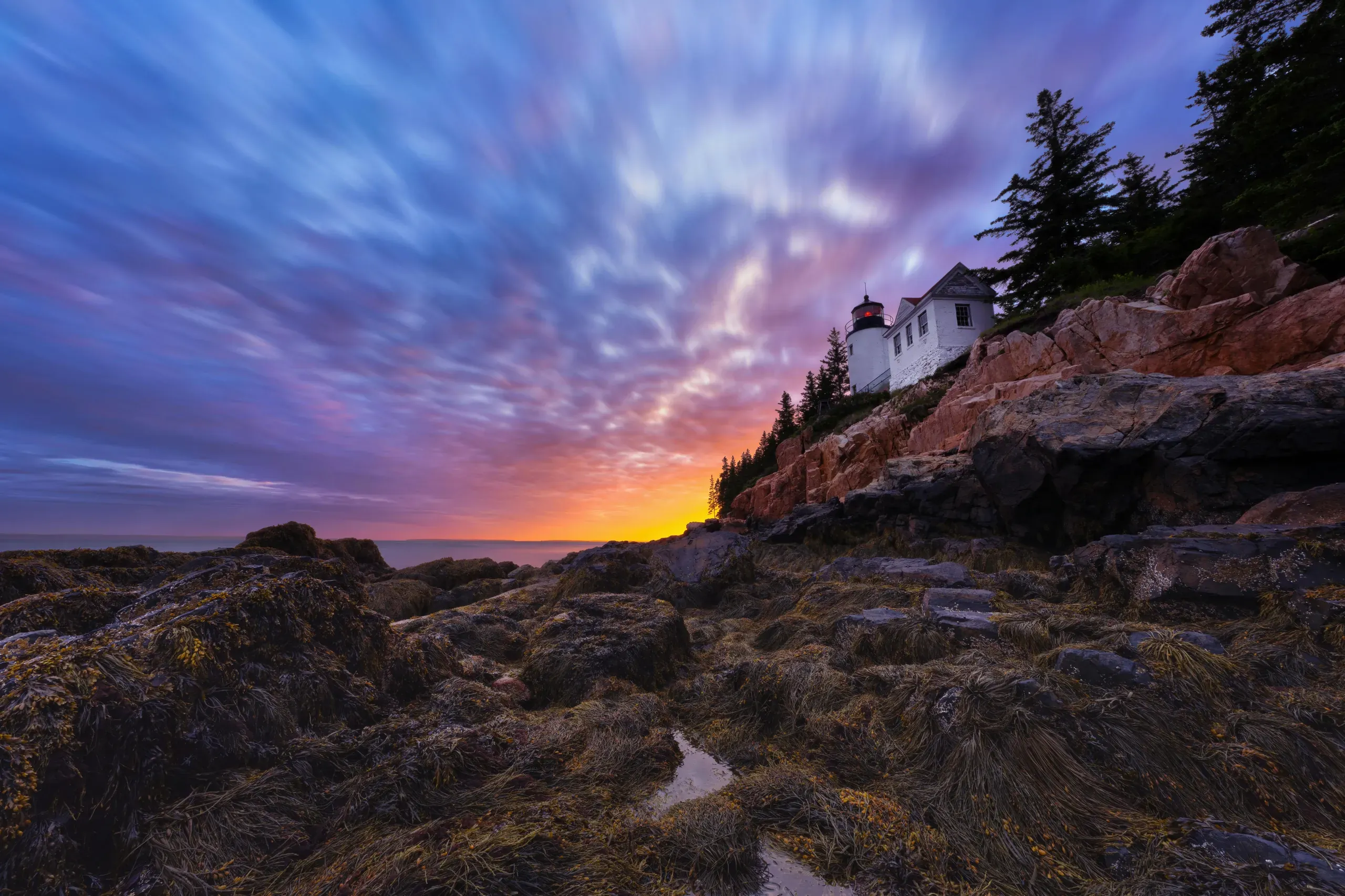 The Bass Harbor Head Lighthouse sits on a rocky hill under a dramatic sky at dusk in Southwest Harbor, Maine.