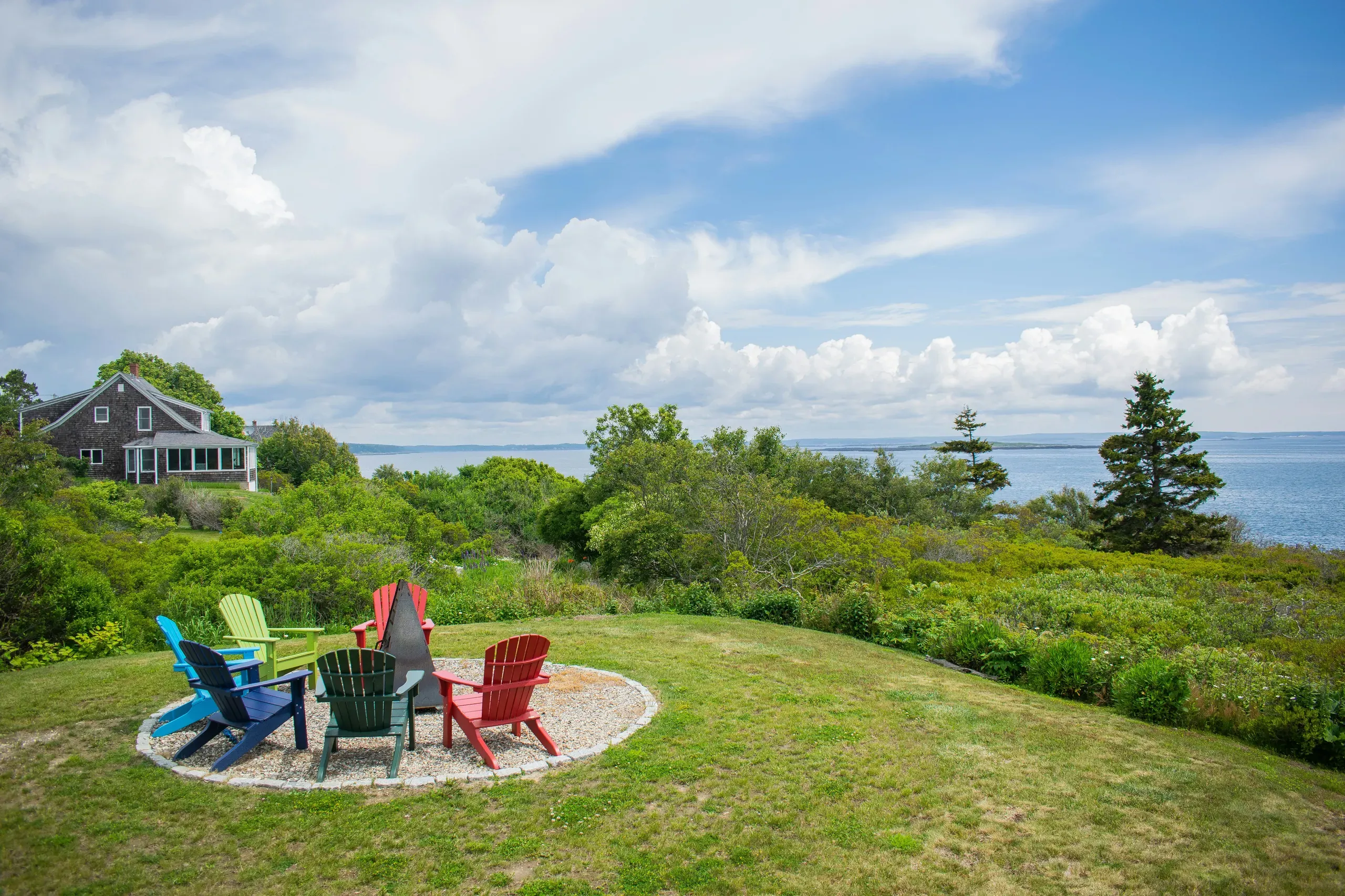 A group of colourful Adirondack lawn chairs sits on a lush green lawn overlooking the water in Harpswell, Maine.