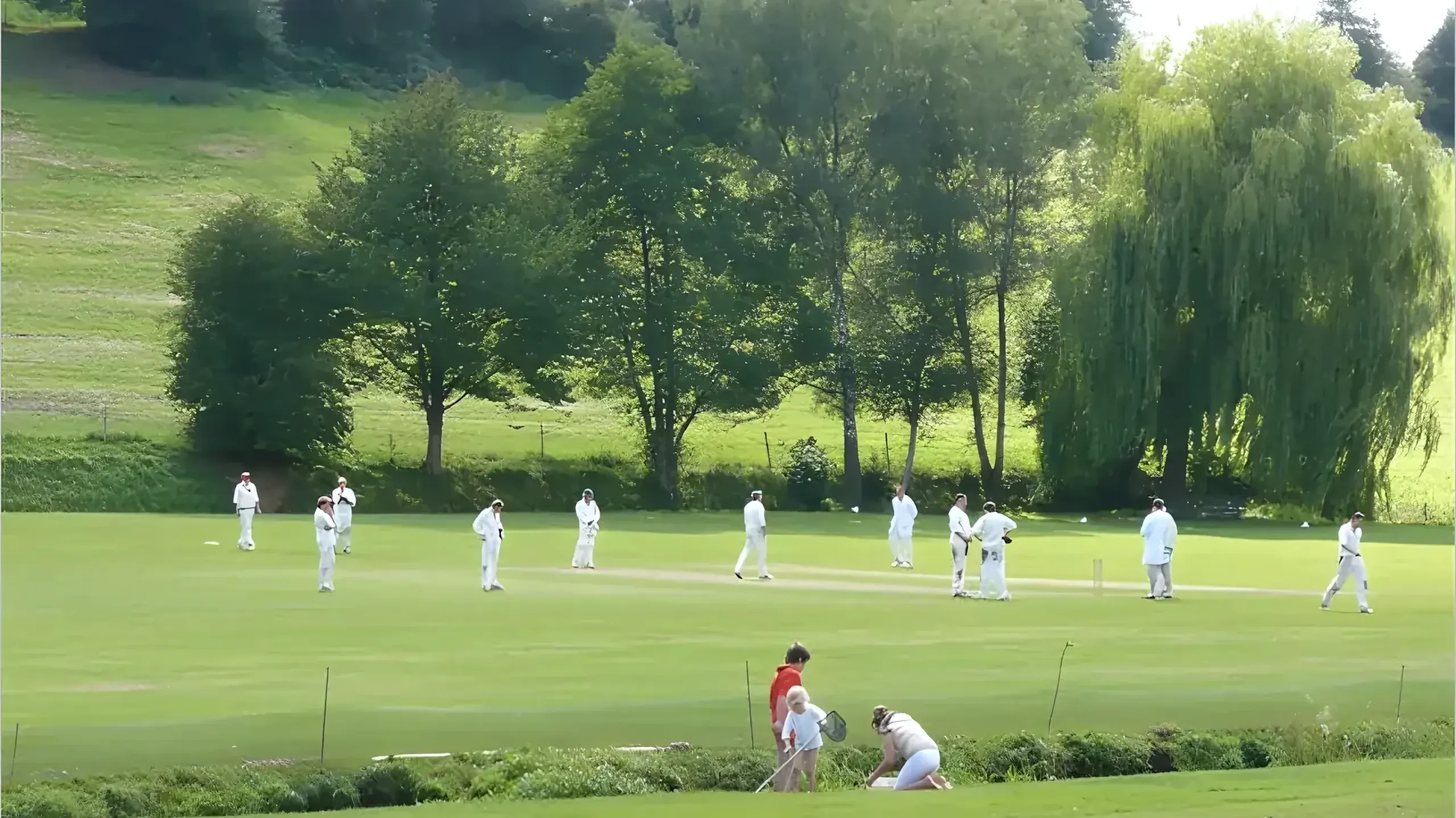 A summer cricket match on the village green in Abinger Hammer, Surrey, with children playing by the stream