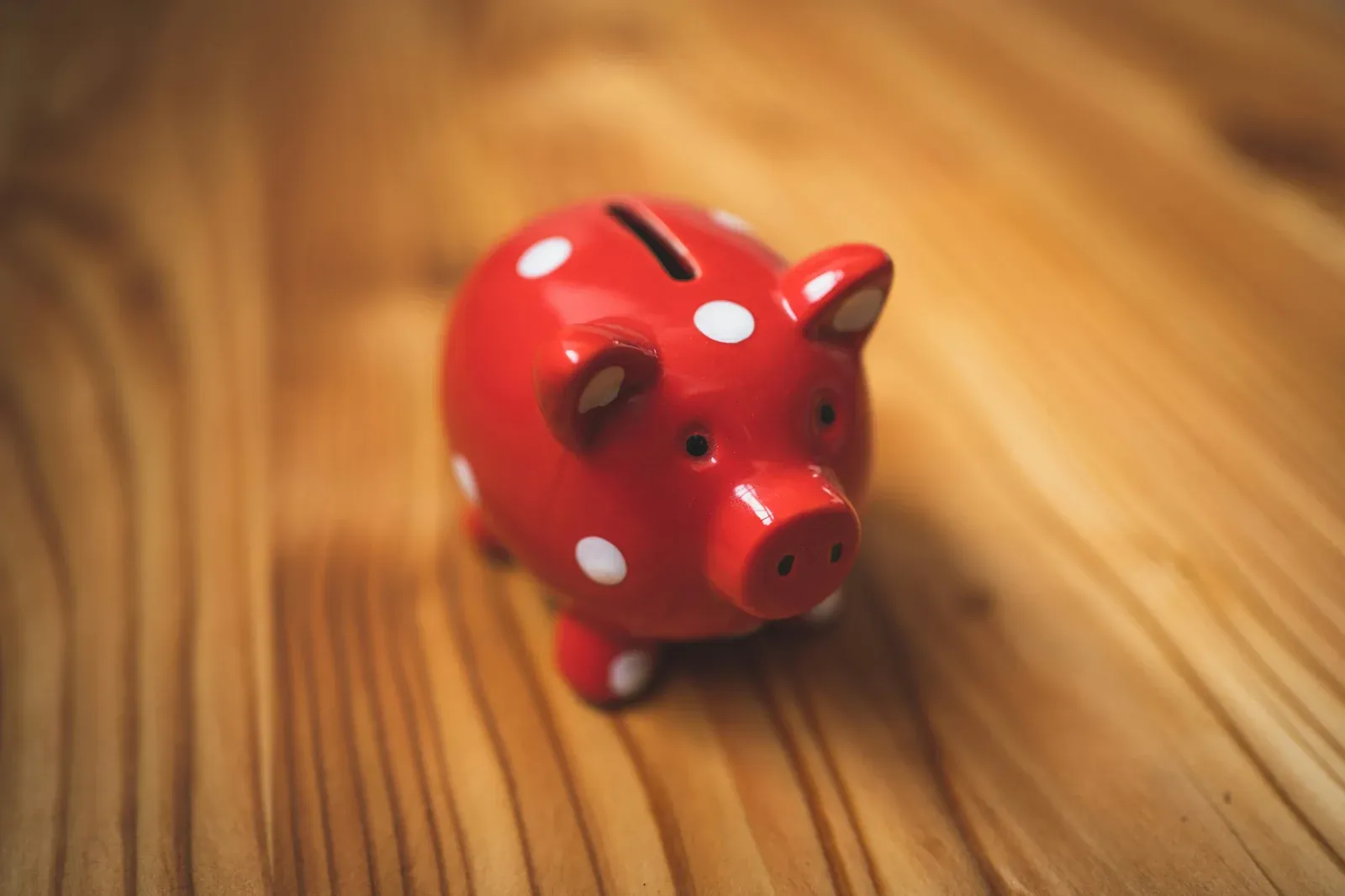 A red ceramic piggy bank with white polka dots on a wooden table