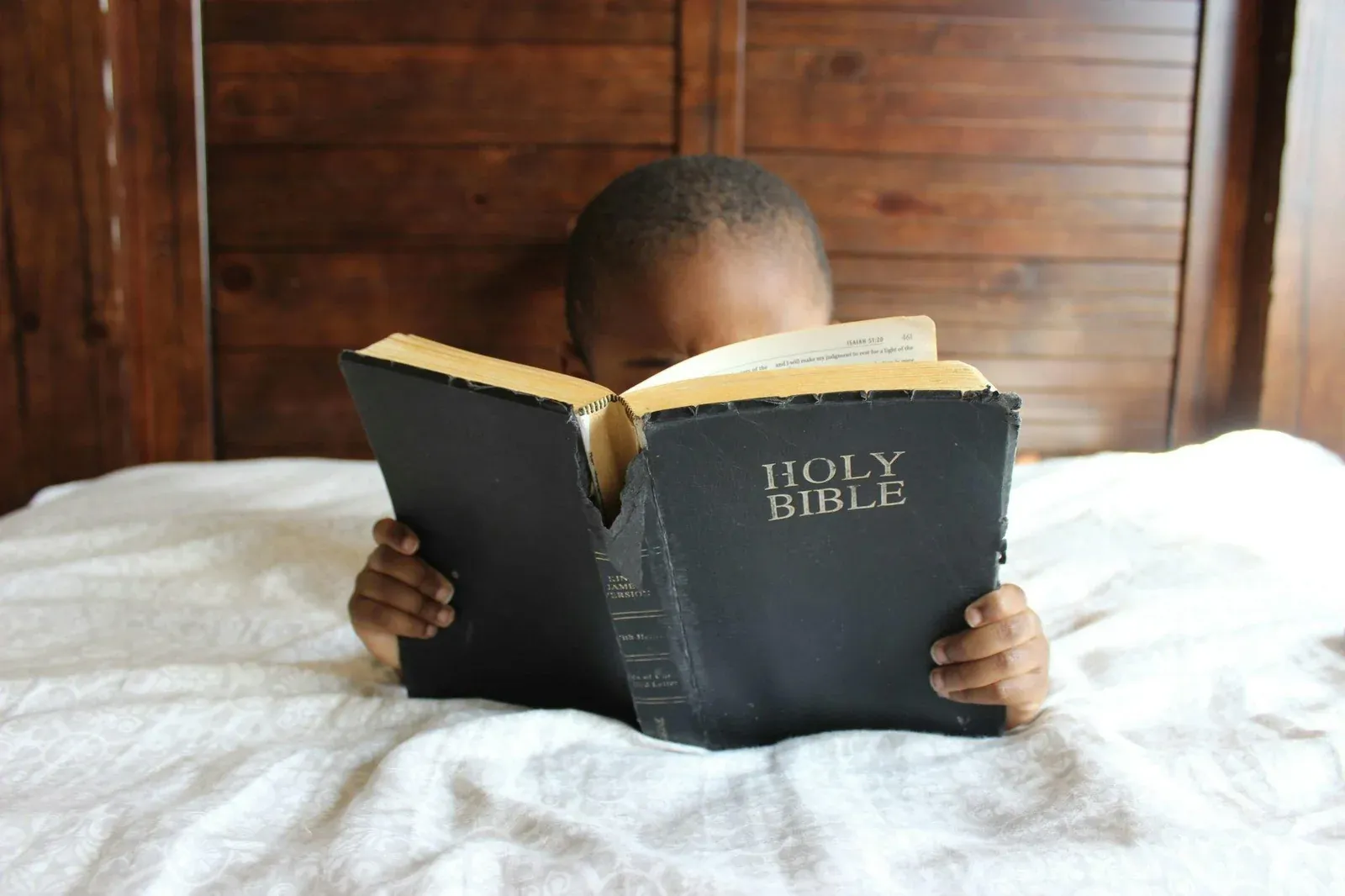 A child reading a well-worn Holy Bible on a bed