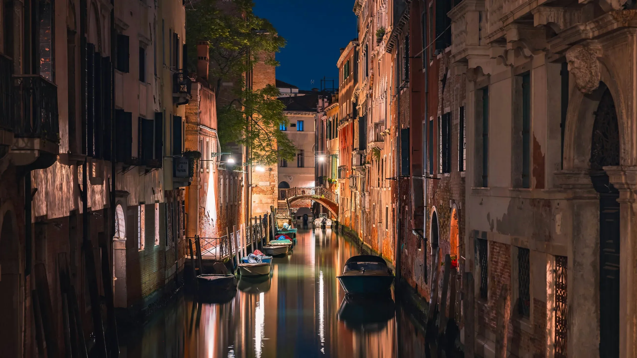 A narrow canal in Venice, Italy at night with illuminated buildings reflected in the water