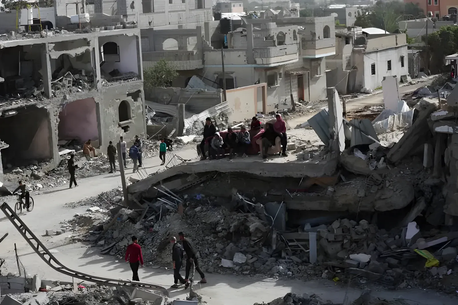 Palestinians walking through a devastated Gaza neighbourhood, a completely collapsed building in the centre surrounded by rubble