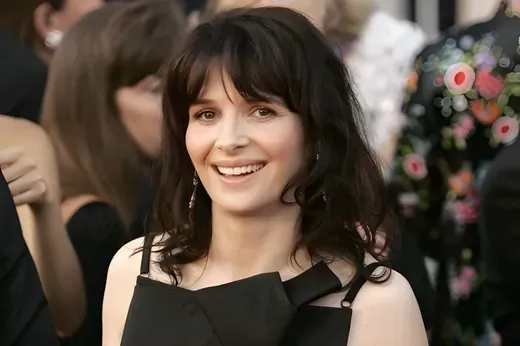 Juliette Binoche smiling at a red carpet event, wearing a black dress with her dark hair loose