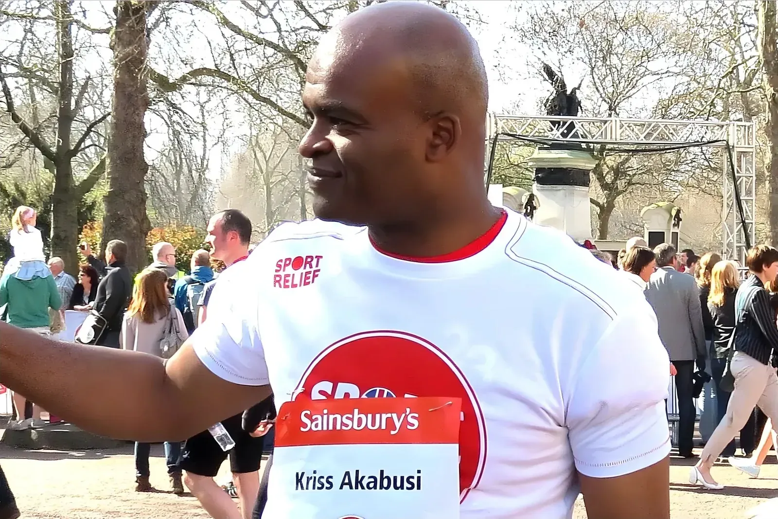 Kriss Akabusi smiling in a Sport Relief t-shirt with a Sainsbury's name badge at a charity run in Hyde Park, London
