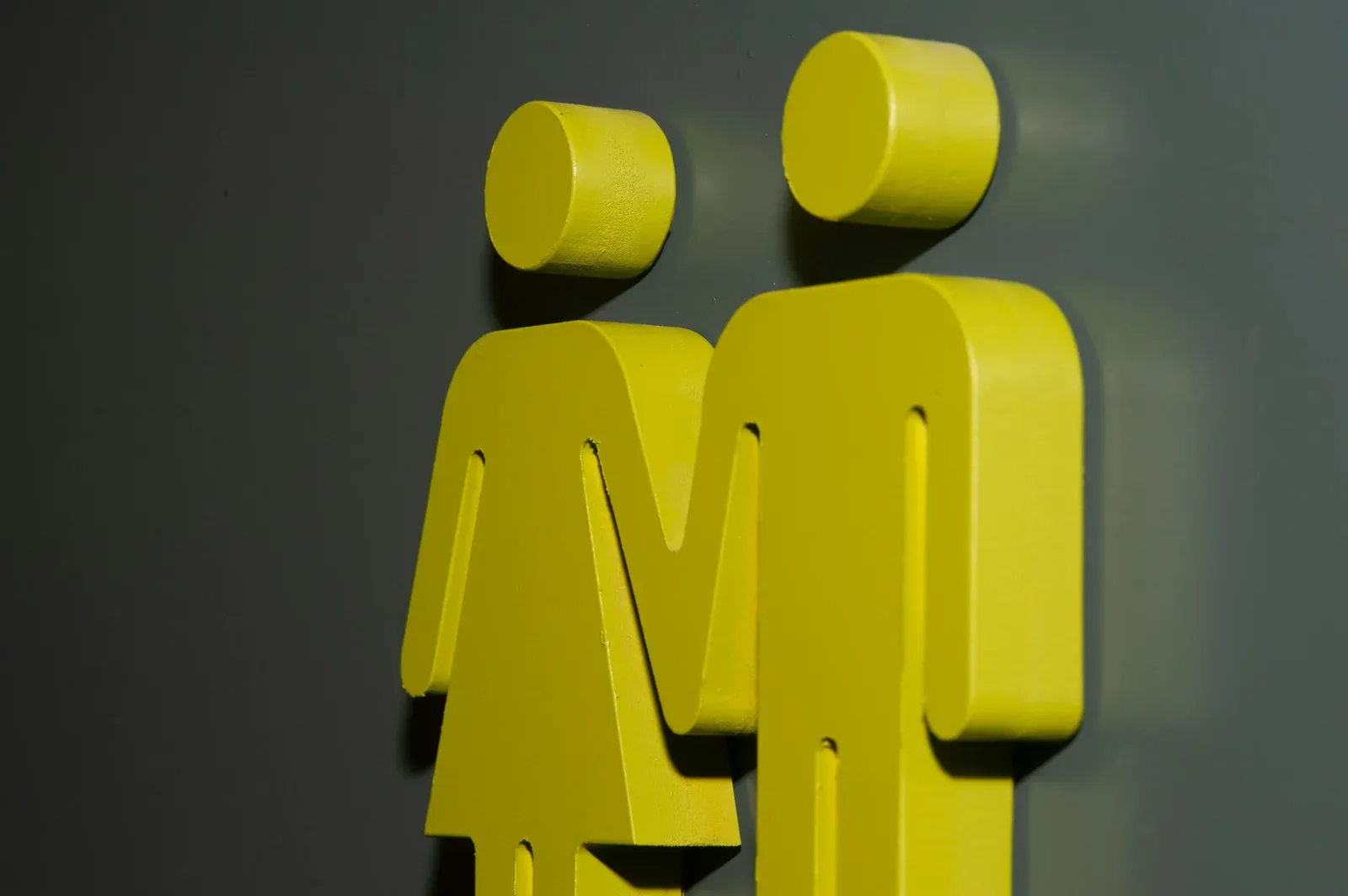 Close-up of yellow 3D male and female bathroom-sign figures mounted on a dark wall