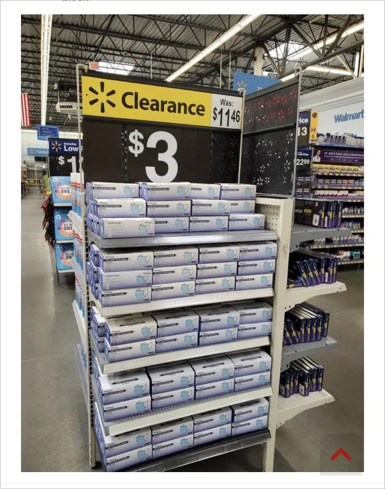 Walmart clearance display showing boxes of disposable face masks marked down from $11.46 to $3, stacked in large unsold quantities on shelves