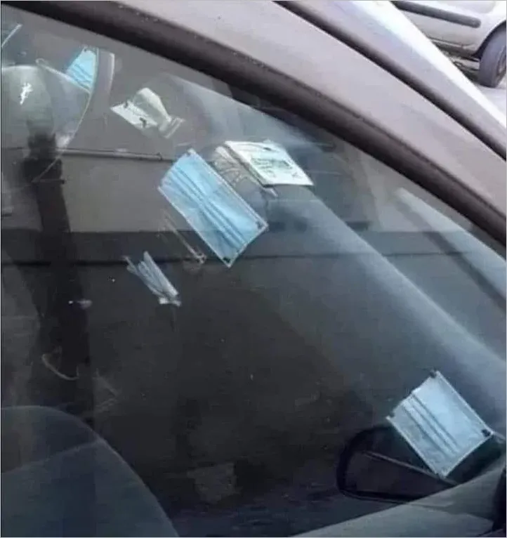 Photo through a car window showing multiple used disposable blue surgical masks scattered across the dashboard and seats of a car