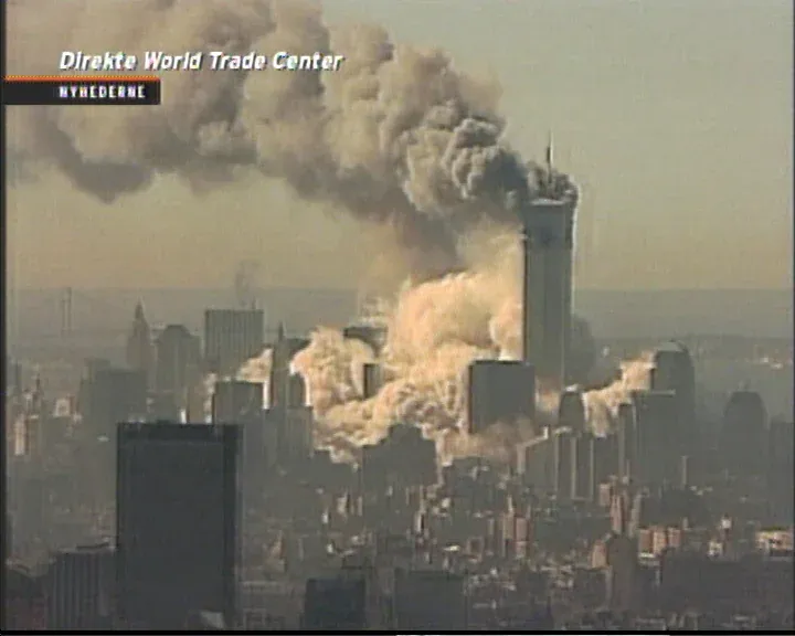Danish Nyhederne TV screenshot showing both WTC towers still standing with heavy smoke, orange-tinted dust and debris around the base, Direkte World Trade Center overlay