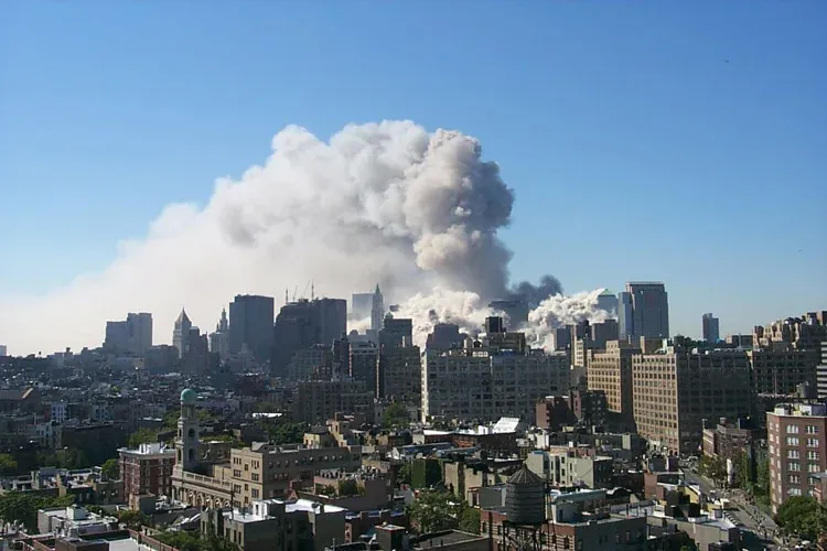Distant view of the WTC dust plume rising over the Manhattan skyline against a blue sky, seen from across the East River