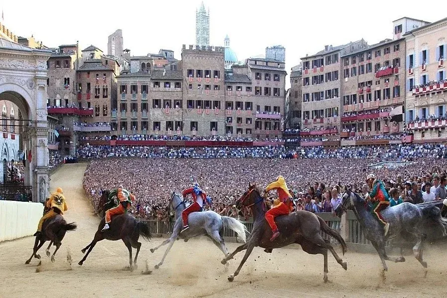 Jockeys racing bareback on horses around the Piazza del Campo during the Palio di Siena, with packed crowds lining the historic buildings