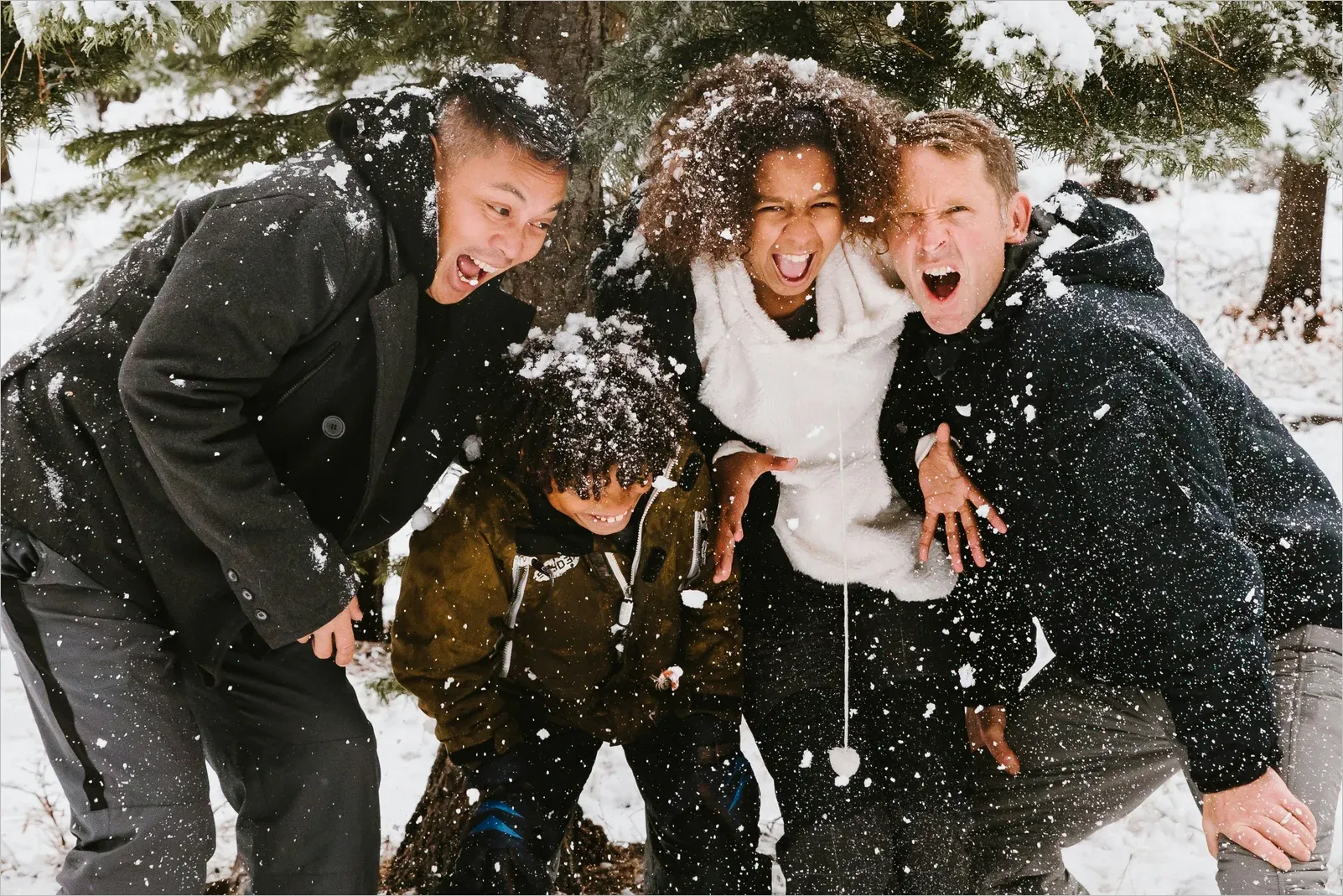 Four friends of different ethnicities laughing together as snow falls around them