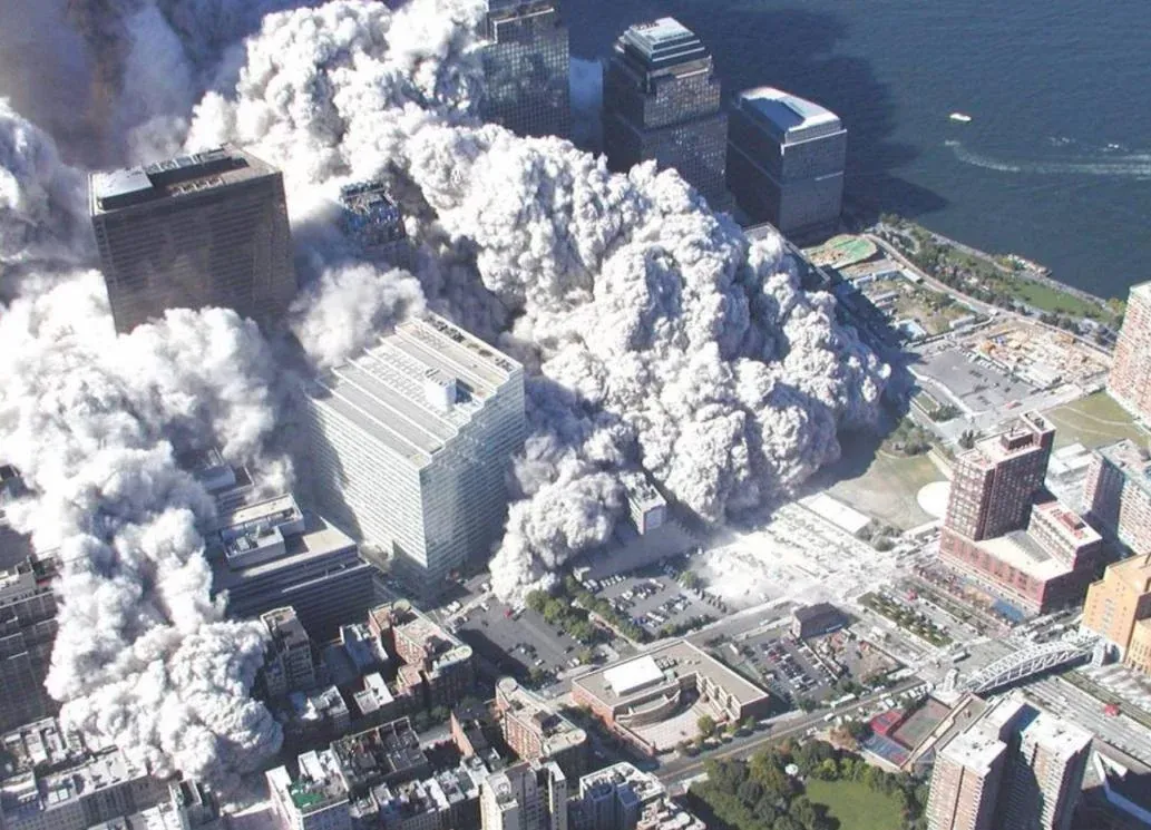 Wide aerial view of massive dust cloud spreading across lower Manhattan toward the Hudson River, surrounding buildings emerging through the white dust
