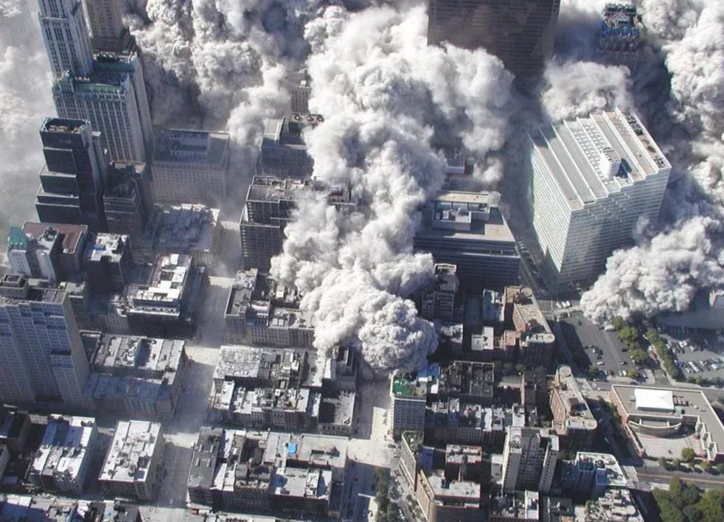 Aerial view looking down at the WTC collapse site with dust billowing through the street grid of lower Manhattan, buildings casting shadows through the haze