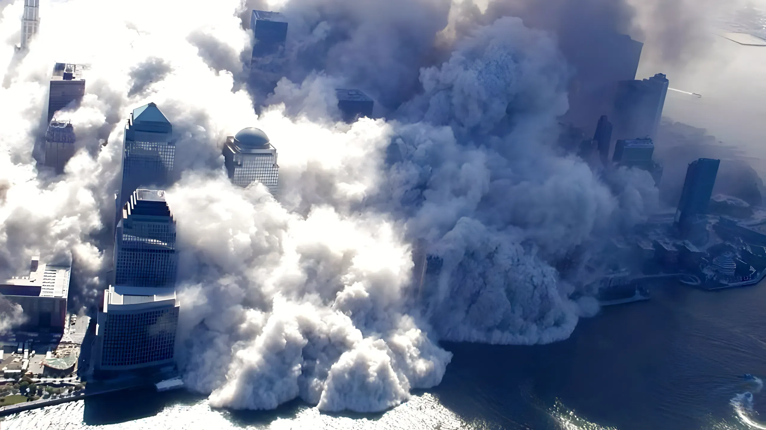 Aerial photograph of the World Trade Center site during collapse, massive clouds of white dust engulfing lower Manhattan and rolling toward the Hudson River