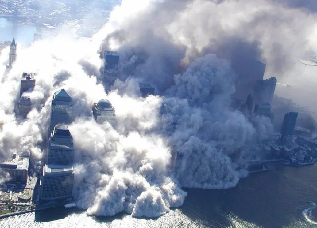 Aerial view from the southwest with World Financial Center towers protruding through an expanding dust cloud that is spilling into the Hudson River