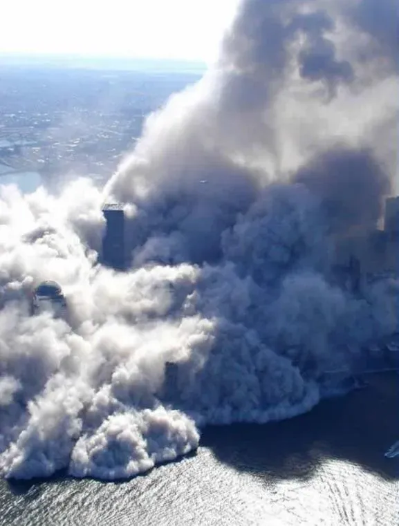 Aerial view from the south showing massive dust cloud completely enveloping lower Manhattan, only the tops of World Financial Center towers still visible, dust spreading over the Hudson River
