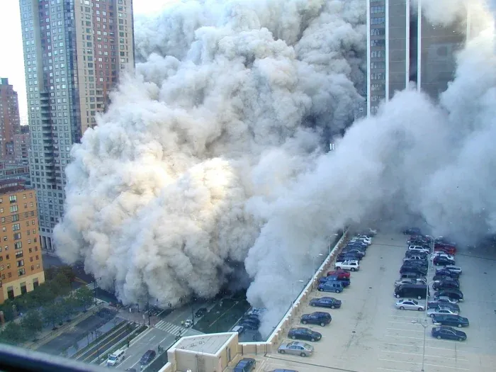 Elevated view of dust cloud advancing through lower Manhattan streets past a parking garage full of cars, residential buildings on left, the cloud resembling a pyroclastic flow
