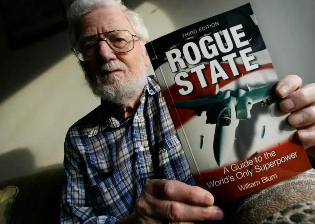 William Blum holding up a copy of his book Rogue State: A Guide to the World's Only Superpower