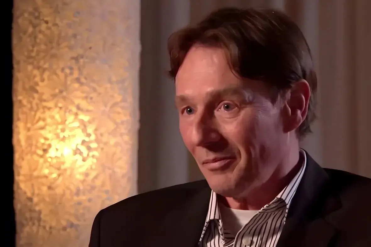 Close-up portrait of Ronald Bernard in a dark jacket and striped shirt, with an ornate lamp glowing behind him