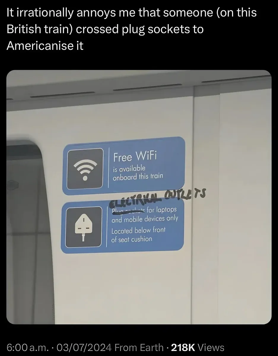 X/Twitter post (6:00 a.m. 03/07/2024 From Earth). Text: "It irrationally annoys me that someone (on this British train) crossed plug sockets to Americanise it". Photo shows British train interior with two blue information signs: "Free WiFi is available onboard this train" and "Plug sockets for laptops and mobile devices only. Located below front of seat cushion." Someone has handwritten "ELECTRICAL OUTLETS" over "Plug sockets" in black marker