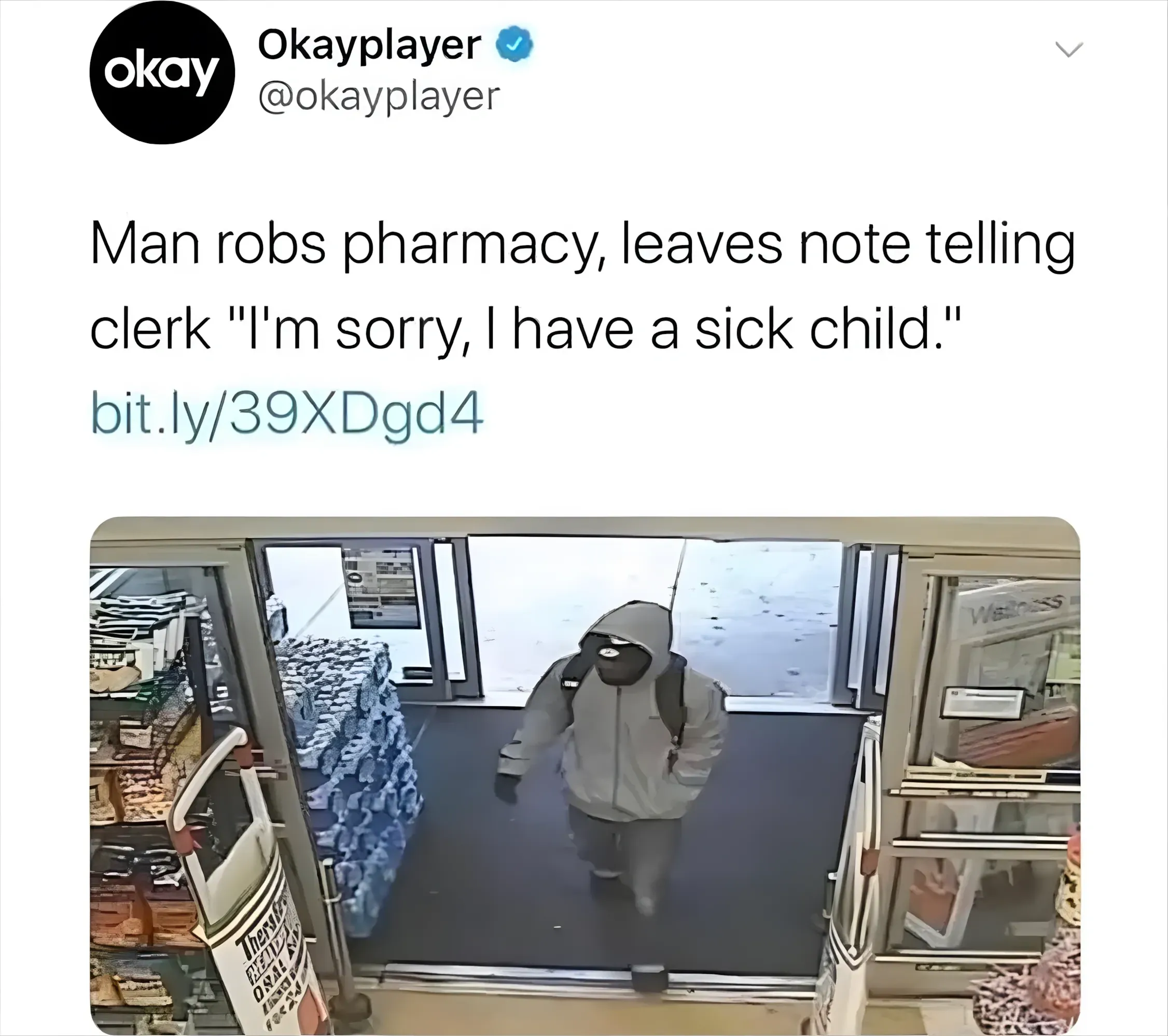 Twitter/X post. Okayplayer (@okayplayer, verified). Tweet: 'Man robs pharmacy, leaves note telling clerk "I'm sorry, I have a sick child."' with link. CCTV screenshot showing hooded figure entering a pharmacy