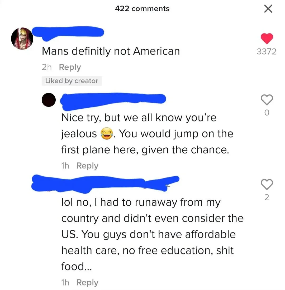 TikTok/Instagram comment thread. First (username redacted, 2h, Liked by creator): "Mans definitly not American". Reply (blue, 1h): "Nice try, but we all know you're jealous. You would jump on the first plane here, given the chance." Reply (blue, 1h): "lol no, I had to runaway from my country and didn't even consider the US. You guys don't have affordable health care, no free education, shit food..."