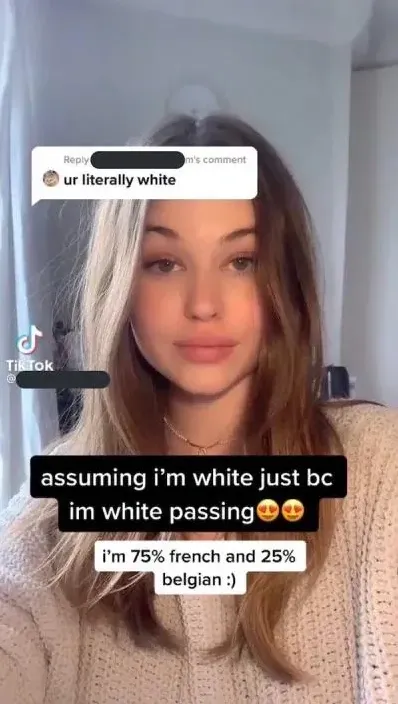 TikTok screenshot. Video of a young white woman with brown hair in a beige knit sweater. Overlaid comment: "ur literally white". Text overlay: "assuming i'm white just bc im white passing" with heart-eyes emojis. Below: "i'm 75% french and 25% belgian :)"