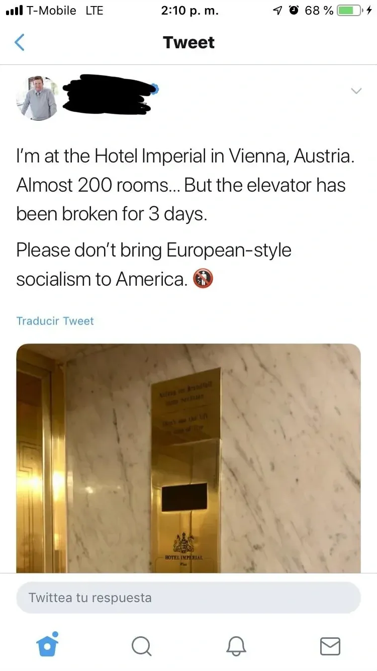 Twitter/X post on mobile (T-Mobile LTE) with Spanish-language interface ("Traducir Tweet", "Twittea tu respuesta"). Tweet (username redacted, profile photo of older man): "I'm at the Hotel Imperial in Vienna, Austria. Almost 200 rooms... But the elevator has been broken for 3 days. Please don't bring European-style socialism to America." with clown emoji. Photo of a Hotel Imperial elevator/lift area with marble walls and brass signage