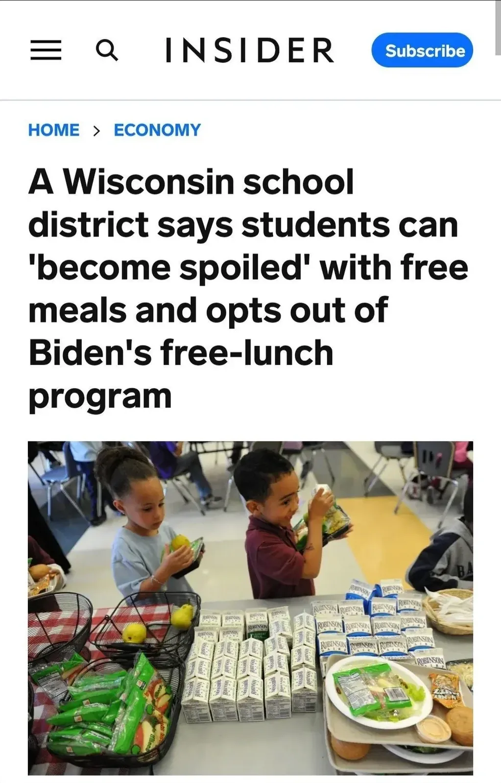 Insider (Business Insider) article screenshot. HOME > ECONOMY. Headline: "A Wisconsin school district says students can 'become spoiled' with free meals and opts out of Biden's free-lunch program". Photo of two young children at a school cafeteria table with lunch trays of food