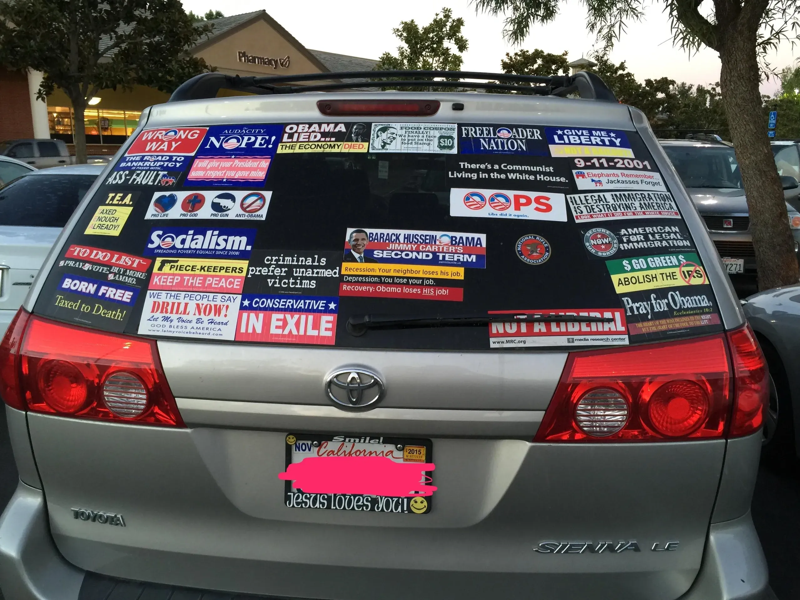 Photo of the rear of a silver Toyota Sienna minivan in a parking lot (pharmacy visible in background). The entire rear window is covered in political bumper stickers including: "WRONG WAY", "NOPE!", "OBAMA LIED THE ECONOMY DIED", "FREELOADER NATION", "GIVE ME LIBERTY", "9-11-2001", "There's a Communist Living in the White House", "OOPS" (Obama logo), "Socialism." (with hammer and sickle), "BARACK HUSSEIN OBAMA SECOND TERM", "ILLEGAL IMMIGRATION", "criminals prefer unarmed victims", "BORN FREE Taxed to Death!", "DRILL NOW!", "CONSERVATIVE IN EXILE", "NOT A LIBERAL", "Pray for Obama", "ABOLISH THE IRS", and many more. License plate redacted. Upside-down "Jesus Loves" sticker on bumper