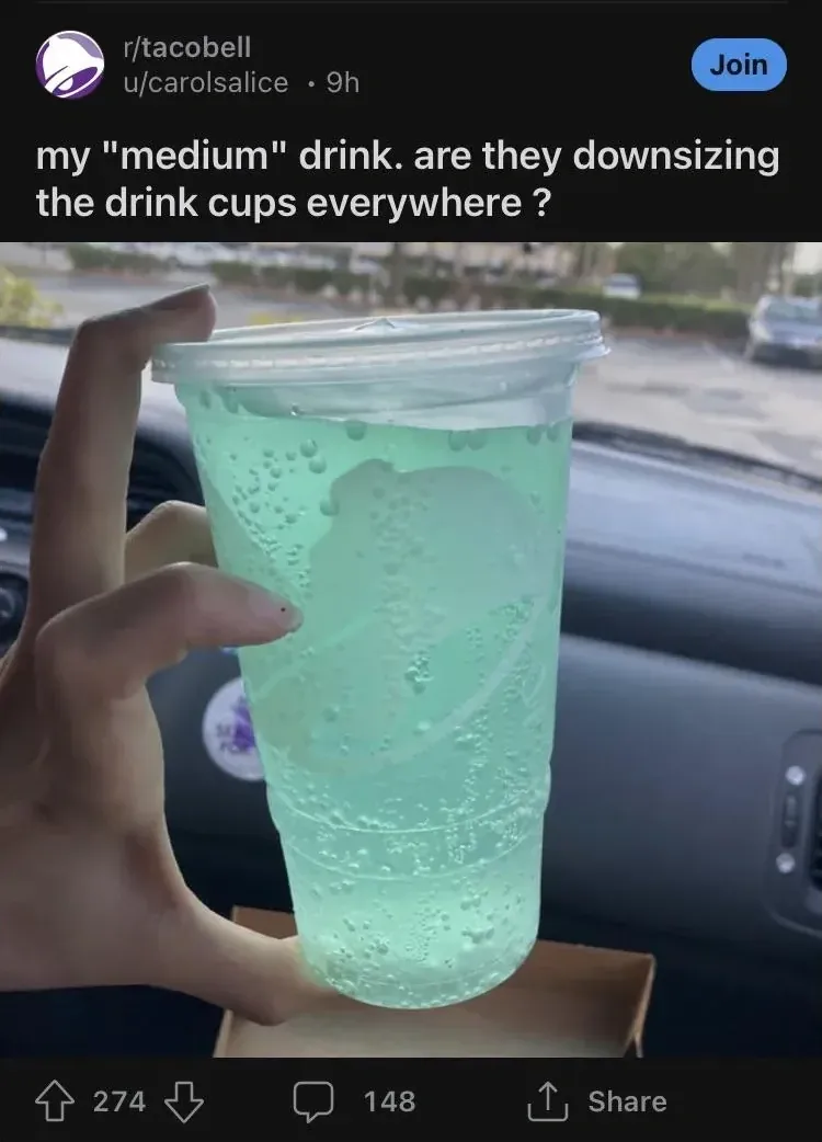Reddit post from r/tacobell by u/carolsalice (9h): "my 'medium' drink. are they downsizing the drink cups everywhere?" Photo shows a hand holding an enormous clear plastic cup filled with bright turquoise-green soda in a car, the cup nearly as long as the person's forearm.