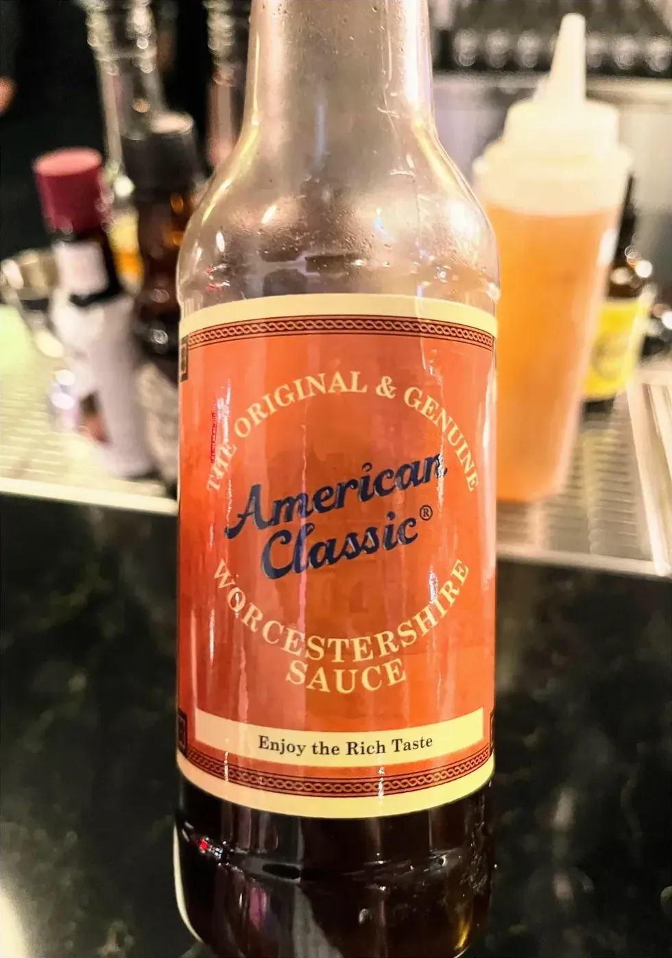 Photo of a bottle of American Classic Worcestershire Sauce with the tagline The Original and Genuine and Enjoy the Rich Taste on a bar counter