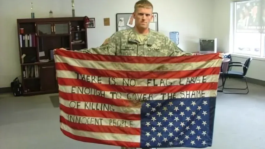 US soldier holding an upside-down American flag with the words 'There is no flag large enough to cover the shame of killing innocent people' written on it