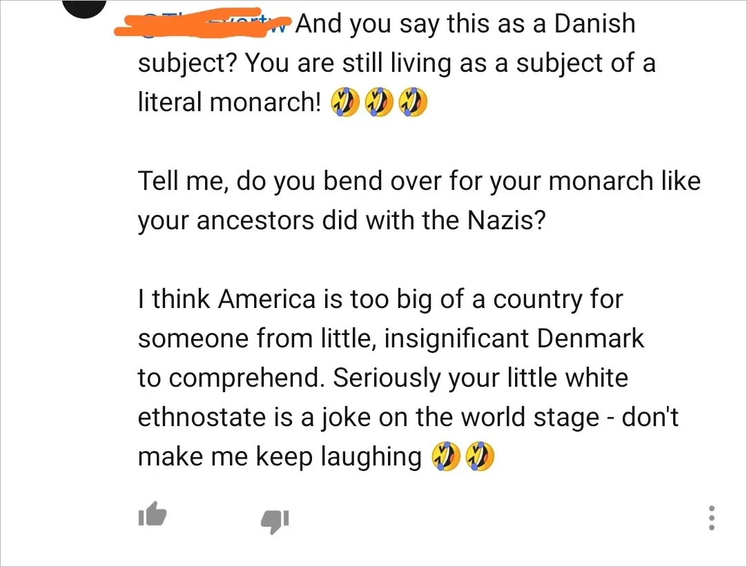 YouTube comment. Username scribbled orange. Text: "And you say this as a Danish subject? You are still living as a subject of a literal monarch! [three laughing-crying emojis] Tell me, do you bend over for your monarch like your ancestors did with the Nazis? I think America is too big of a country for someone from little, insignificant Denmark to comprehend. Seriously your little white ethnostate is a joke on the world stage - don't make me keep laughing [two laughing-crying emojis]" Thumbs up/down buttons visible.