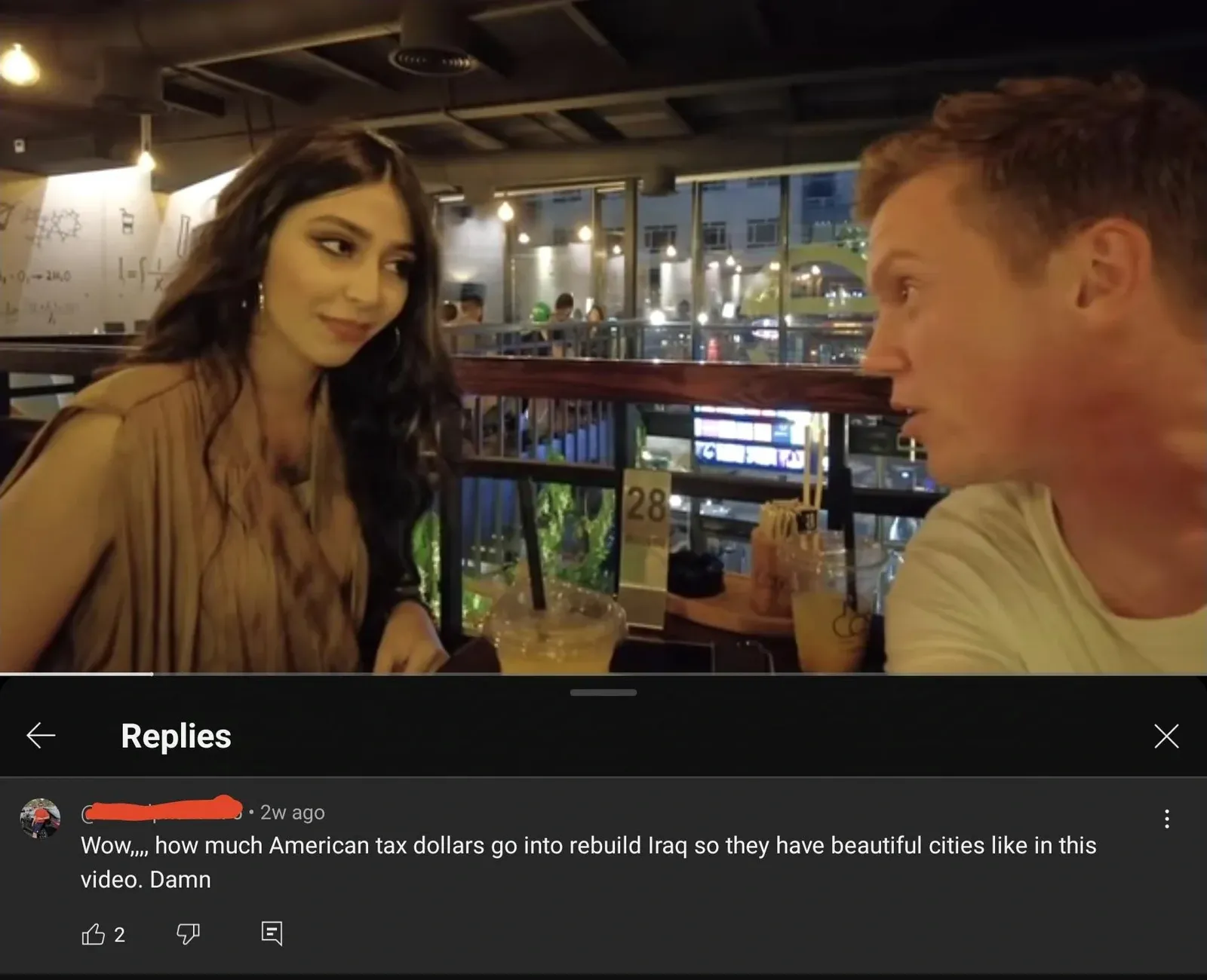 YouTube/TikTok comment section. Video still shows a man and woman at a stylish bar/restaurant, appears to be in Iraq. Comment (2w ago): Wow... how much American tax dollars go into rebuild Iraq so they have beautiful cities like in this video. Damn