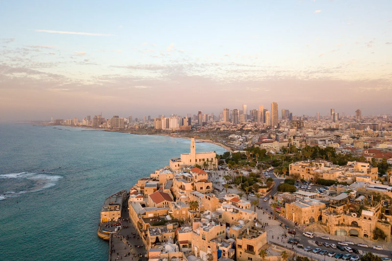 Aerial view of old Jaffa and the Tel Aviv coastline at sunset, sandstone buildings in the foreground with modern skyscrapers along the shore
